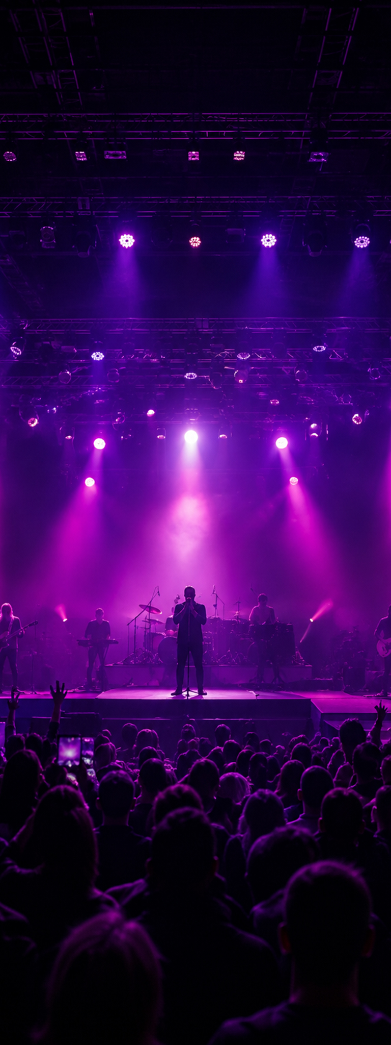 Live-Konzert mit Band auf einer großen Bühne vor ausverkauftem Publikum und eindrucksvoller Lichtshow in violetten Farben.